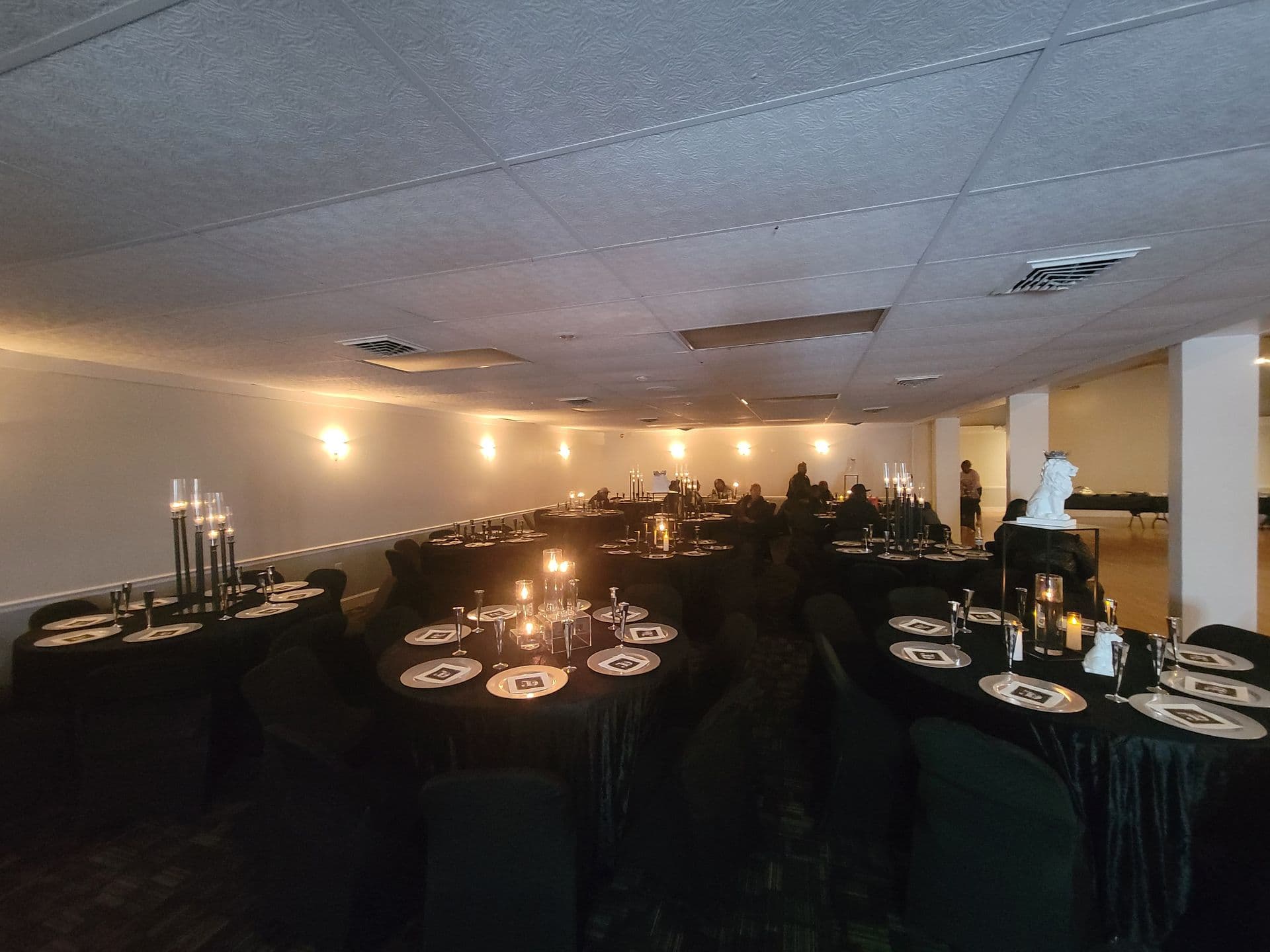 Banquet hall prepared for an evening event with dark linens, candlelight, and round tables